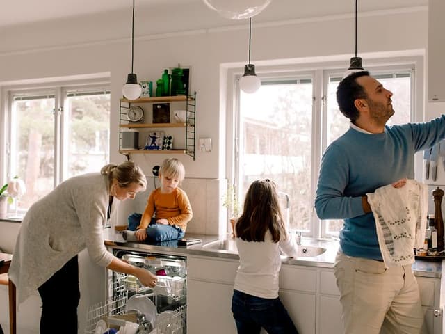 Familj i ett kök som tar ut ren disk ur diskmaskinen.