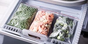 Tre plastpåsar med infrysta grönsaker i en frys