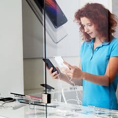En ung kvinne holder opp og sammenligner smarttelefoner i en butikk