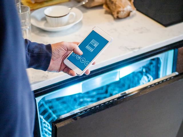 En mann holder en smarttelefon foran en åpen oppvaskmaskin