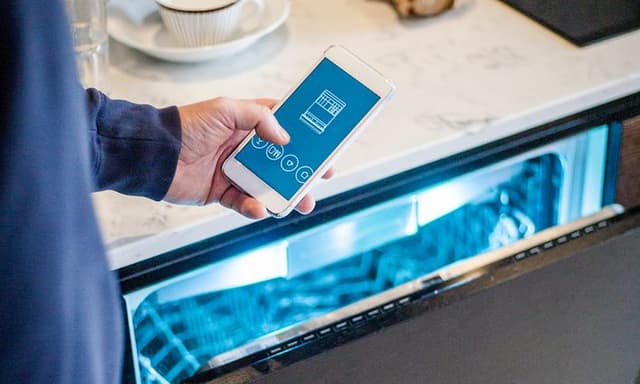 En mann holder en smarttelefon foran en åpen oppvaskmaskin