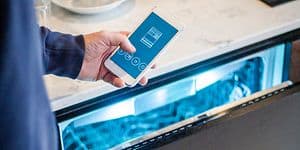 En mann holder en smarttelefon foran en åpen oppvaskmaskin