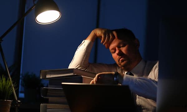 mann ser på klokke med et oppgitt ansiktsuttrykk over et rotete skrivebord
