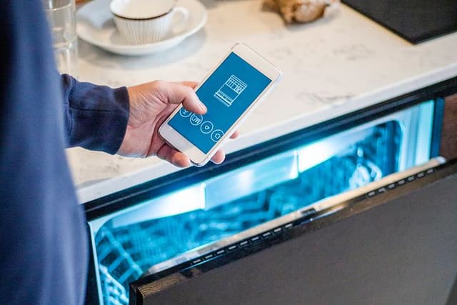 Man håller sin smartphone framför en halvöppen diskmaskin med belysning