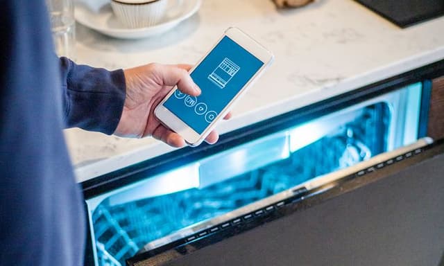 Man håller sin smartphone framför en halvöppen diskmaskin med belysning