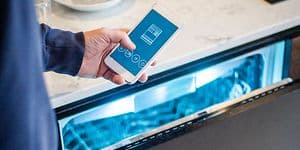 Man håller sin smartphone framför en halvöppen diskmaskin med belysning