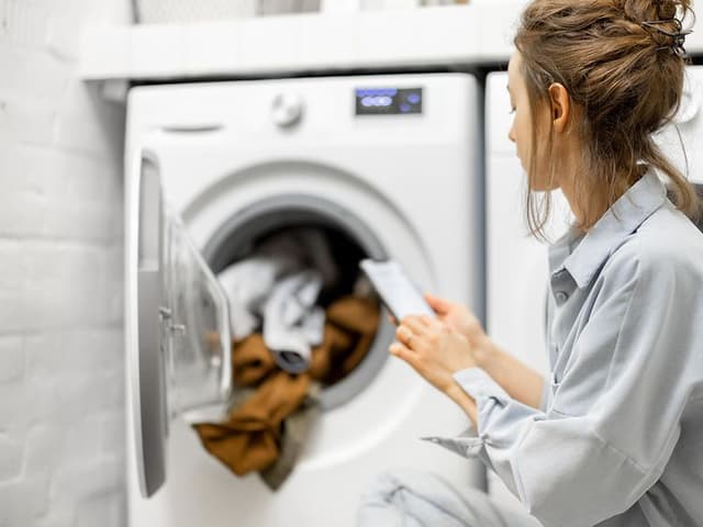 En kvinne sjekker smarttelefonen sin foran en vaskemaskin