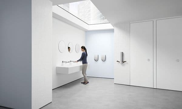 Kvinna som tvättar händerna på en offentlig toalett med Dyson AirBlade-torkar intill