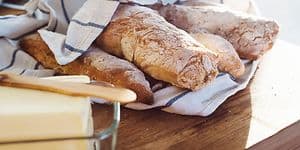 Flera nybakade bröd inuti en kökshandduk och smör bredvid