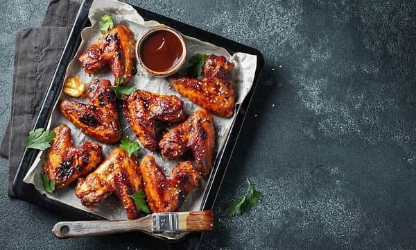 Stekplåt med grillade kycklingvingar, grillpensel och sås