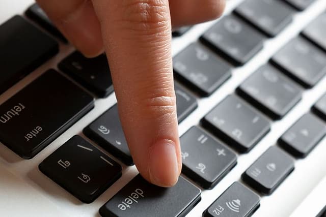 En hand som trycker på delete-knappen på en bärbar dator