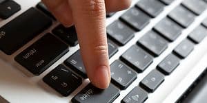 En hand som trycker på delete-knappen på en bärbar dator