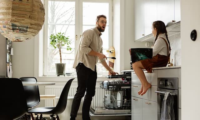 Mies laittaa ruokailuvälineitä astiapesukoneen erilliselle aterintasolle