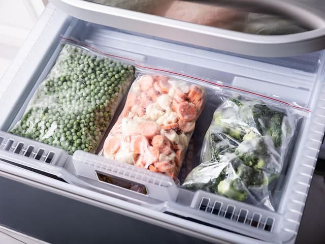 Tre plastposer med frosne grønnsaker i en fryser