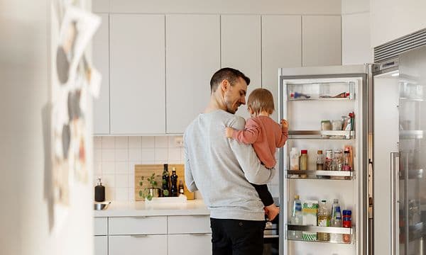 En mann holder et barn foran kjøleskapet på kjøkkenet