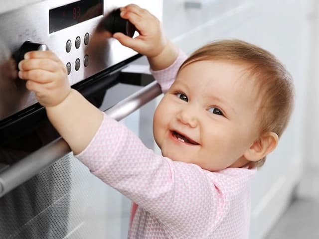 Smilende baby som griper vriderne på stekeovn
