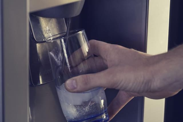En hånd fyller i et glass vann fra vanndispenseren