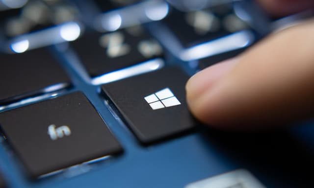 Finger som trykker på Microsoft Windows-tast på blå bærbar PC