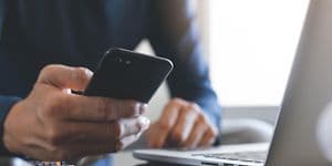 Nærbilde av en person som holder en smarttelefon foran en bærbar PC