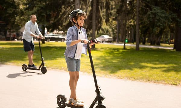 Wearables - Ung kille som åker elsparkcykel med sin pappa i bakgrunden