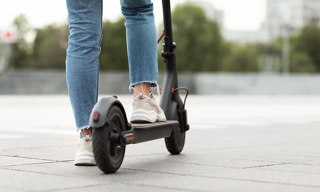 Wearables - Person som har stannat med elsparkcykel med en fot på marken och andra på sparkcykeln sett bakifrån