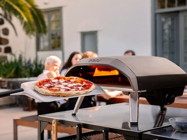 en pizza foran en pizzaovn og mennesker i bakgrunnen