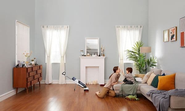 Roborock Dyad trådløs støvsuger i et rom, og en mor som leker med barnet sitt på en sofa