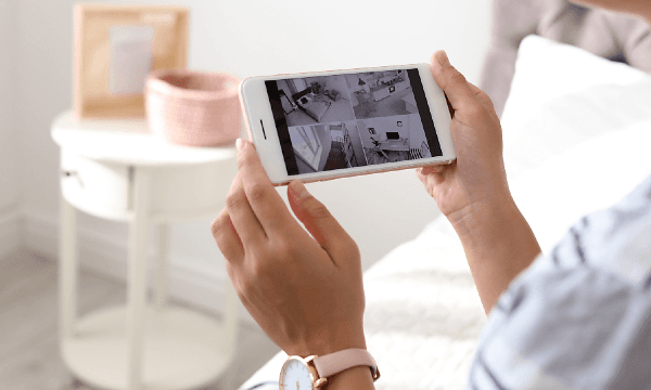 Nainen pitelee iPhonea kädessään ja katselee turvakameran kuvaa sen näytöltä