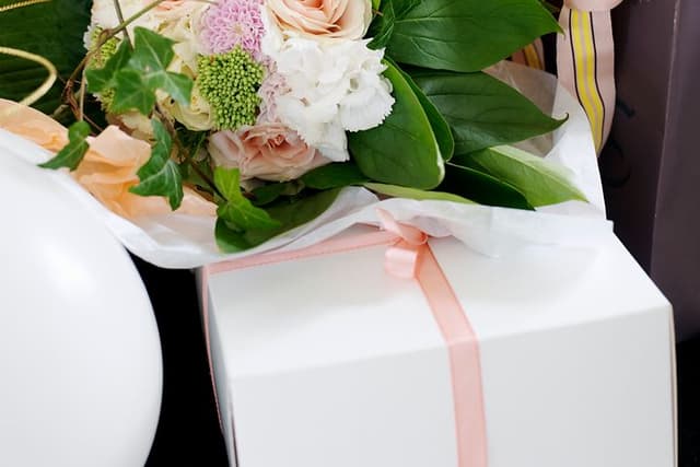 Blomsterbukett og hvit gaveboks med rosa bånd