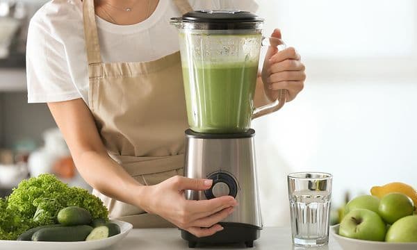 Kvinne som lager grønn smoothie i en blender