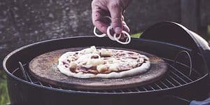Person som putter topping på en pizza
