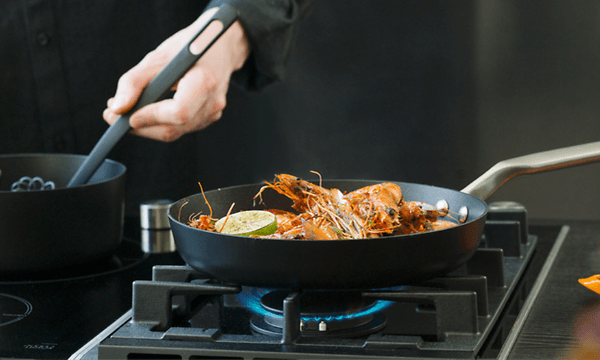 person lager mat med Fiskars Rotisser kaserolle og stekepanne