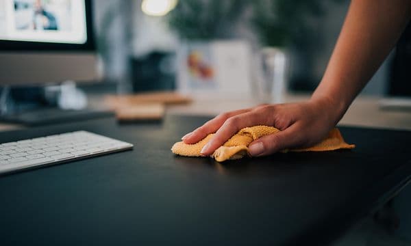 A hand cleaning a black desk with a cloth