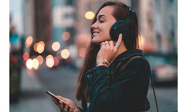 Kvinne med hodetelefoner og smarttelefon smiler