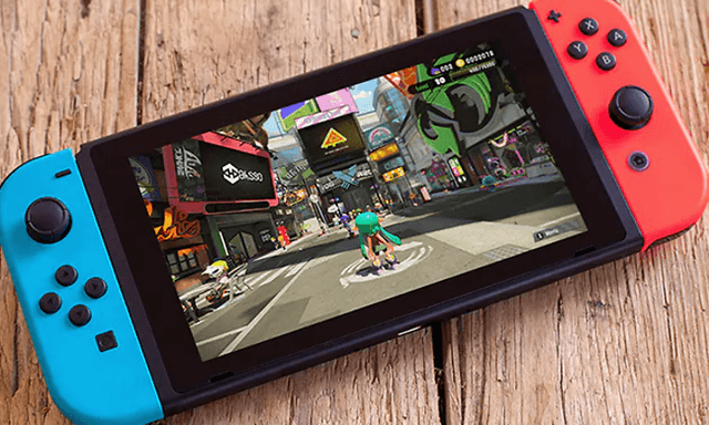 Nintendo Switch enhet, som är blå på ena sidan och röd på andra, placerad på ett träbord. 