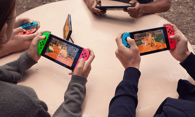 Fyra personer som sitter vid ett runt bord och spelar Nintendo Switch med var sin handhållen enhet.