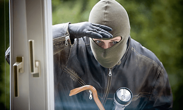 Maskert person med lommelykt ser inn gjennom vindu