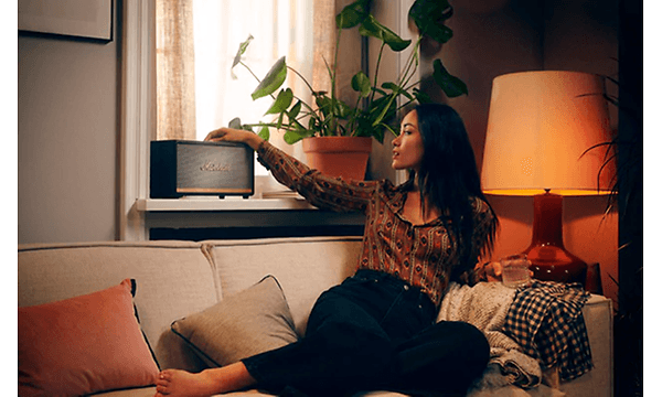 Kvinna sitter i sin soffa och trycker på sin högtalare i fönsterkarmen.