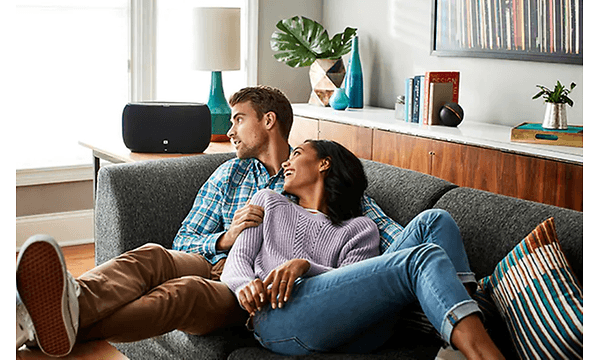 En man och en kvinna myser i soffan och ser mot sin högtalare.