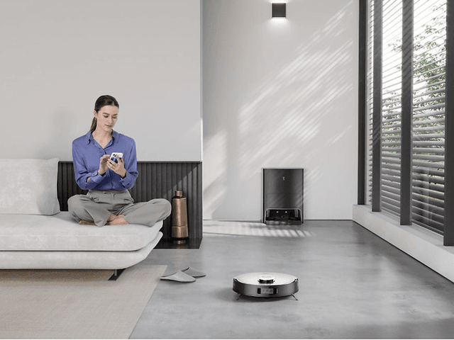 Ecovacs Deebot X1 på et gulv ved siden av en kvinne i en sofa