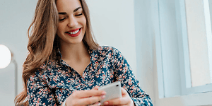Kvinne smiler og ser ned på mobiltelefon
