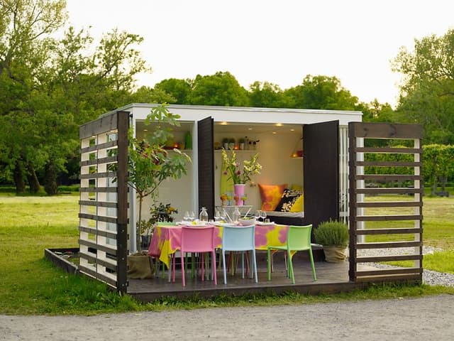 Uppdukat till fest på en paviljong i trädgården med färgglada stolar och en massa blommor.