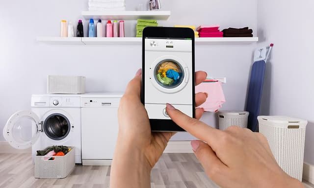 Hånd holder smarttelefon foran en vaskemaskin