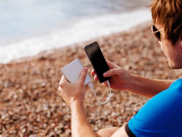Mann på strand som lader smarttelefon med powerbank
