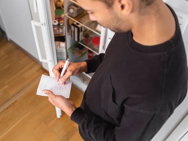 Mann noterer foran åpent kjøleskap