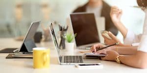 Nærbillede af et bord med personer som arbejder og bærbare computere i dagslys