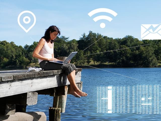Netværk Kvinde sidder udenfor ved en sø og arbejder med sin laptop på skødet