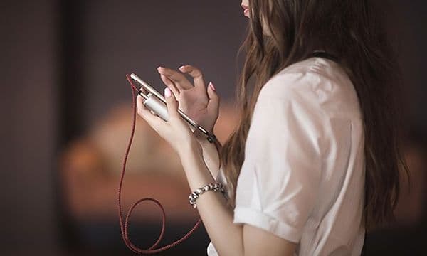 Telecom - En kvinde står og bruger sin smartphone mens den lader fra en powerbank