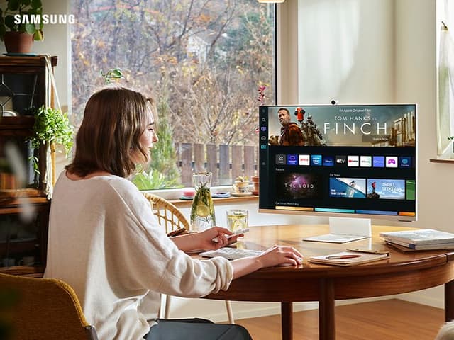 Kvinne som sitter ved spisebord og bruker en Samsung Smart Monitor