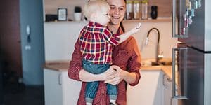 Isä pitelee pientä poikaansa sylissään, joka tutkii jääkaapin oveen kiinnitettyjä magneetteja